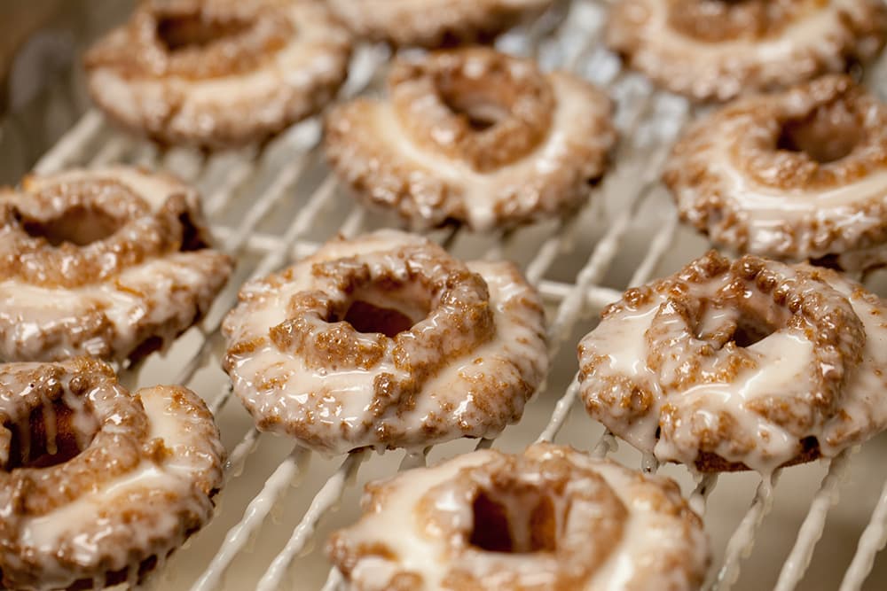 Old Fashioned Donuts being glazed on a sheet rack.